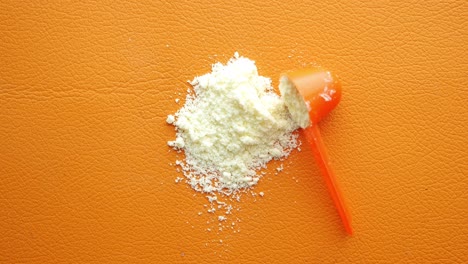 Close-up-of-baby-milk-powder-and-spoon-on-orange-background