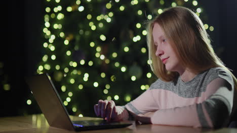 A-teenage-girl-uses-a-laptop-on-the-background-of-a-Christmas-tree