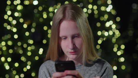 A-teenage-girl-uses-a-smartphone-on-the-background-of-a-Christmas-tree