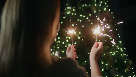 Happy-woman-holding-sparklers,-standing-against-the-backdrop-of-a-Christmas-tree-at-home.-Rear-view