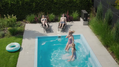 A-group-of-young-people-relax-by-the-pool,-mother-and-daughter-jump-into-the-water