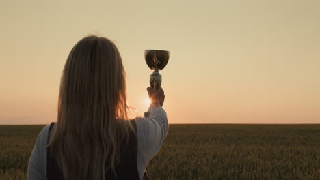 Farmer-woman-raising-champion-cup-in-wheat-field-at-sunset