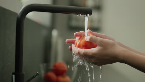 Juicy-red-tomato-is-washed-under-water-from-the-kitchen-tap.-Slow-motion-4k-video