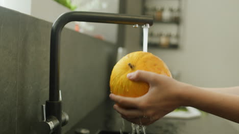 A-woman-washes-a-ripe-melon-under-the-kitchen-faucet