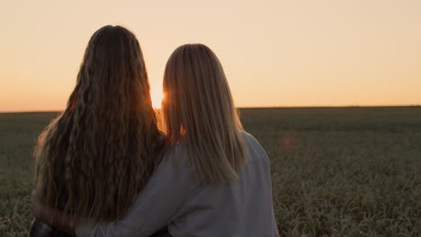Zwei-Frauen-Bewundern-Den-Sonnenuntergang-über-Einem-Weizenfeld,-Rückansicht