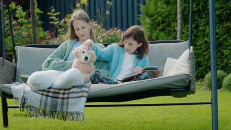 Two-girlfriends-are-relaxing-in-the-garden-at-the-backyard-of-the-house,-playing-with-a-cute-puppy.-Sitting-on-a-garden-swing