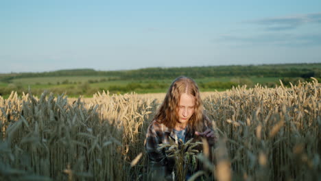 A-teenage-girl-with-long-hair-and-a-bouquet-of-spikelets-of-wheat-sits-in-a-wheat-field.-Summer-on-the-farm