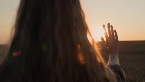 A-girl-with-beautiful-long-hair-holds-out-her-hand-to-the-setting-sun.
