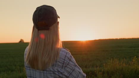 Rear-view-of-a-woman-admiring-the-sunrise-over-a-field-of-wheat