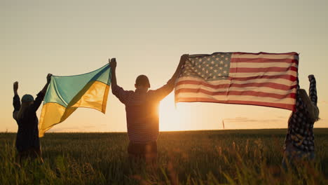 Young-people-raise-up-the-American-and-Ukrainian-flags-against-the-background-of-a-wheat-field-where-the-sun-rises