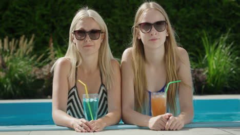 Portrait-of-a-mother-with-a-teenage-daughter.-Together-they-relax-in-the-pool,-drink-refreshing-cocktails.
