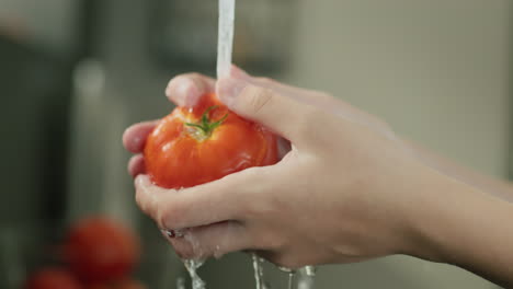 Woman-washing-ripe-tomato-under-running-water-in-the-kitchen