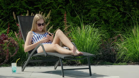 A-teenager-is-relaxing-on-a-sun-lounger-by-the-pool.-Uses-a-smartphone