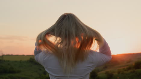A-young-woman-straightens-her-hair,-stands-in-a-picturesque-place-at-sunset