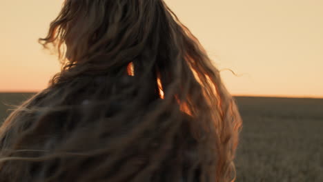 Teenage-girl-with-long-hair-quickly-rotates-her-head-at-sunset,-plays-with-her-hair