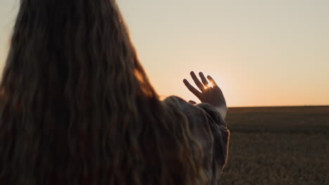 Cute-girl-with-beautiful-long-hair-holds-out-her-hand-to-the-setting-sun.