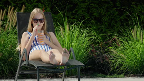 Teenage-girl-relaxing-on-a-sun-lounger-by-the-pool,-drinking-a-cocktail