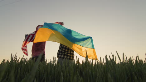 Young-couple-with-usa-and-ukraine-flags-in-wheat-field.-Low-angle-view