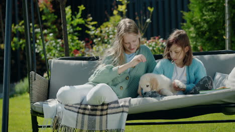 Sisters-play-with-a-little-golden-retriever-puppy.-Sitting-in-a-garden-swing-in-the-backyard-of-a-house