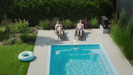 Junges-Paar-Entspannt-Sich-Am-Pool,-Liegt-Auf-Sonnenliegen-Und-Nimmt-Ein-Sonnenbad