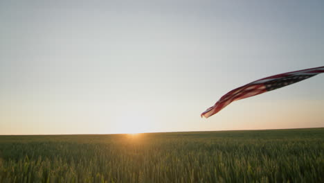 Ein-Amerikanischer-Bauer-Schwenkt-Die-US-Flagge-Vor-Dem-Hintergrund-Eines-Weizenfeldes,-Auf-Dem-Die-Sonne-Aufgeht.-POV-Ansicht
