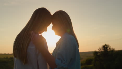 Profile-of-a-woman-with-a-teenage-daughter.-Standing-at-sunset,-mother-gently-touches-the-child
