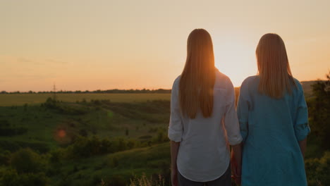A-woman-with-her-teenage-daughter-admire-the-sunset-in-a-picturesque-valley.-Back-view