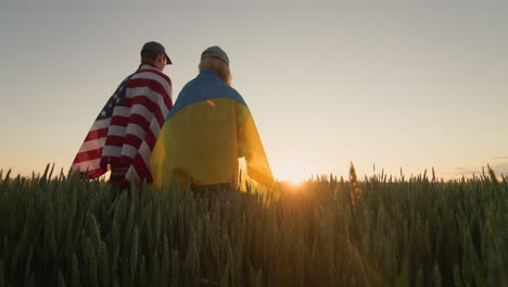 Young-couple-with-usa-and-ukraine-flags-in-wheat-field.-Low-angle-view