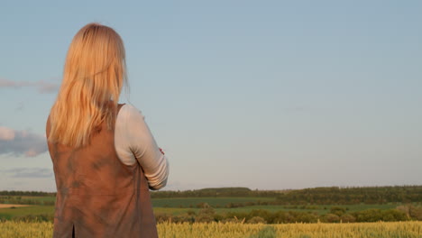 A-woman-looks-at-a-picturesque-landscape-with-a-field-of-wheat.-Back-view