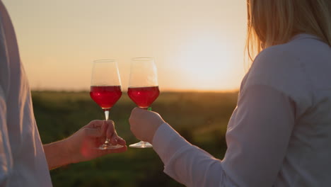 Hands-with-glasses-of-red-wine-clink-against-the-background-of-the-valley-where-the-sun-sets