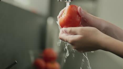 Juicy-ripe-tomato-is-washed-under-water-from-the-kitchen-tap