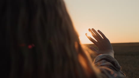 A-girl-with-beautiful-long-hair-holds-out-her-hand-to-the-setting-sun.-Back-view
