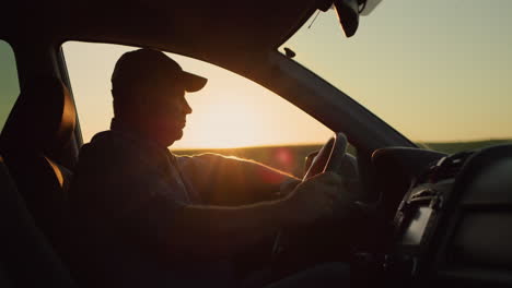 Silhouette-of-a-male-driver-driving-a-car.-Looks-ahead-at-the-background-of-the-field-where-the-sun-sets