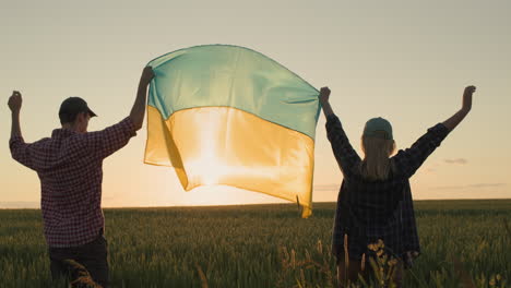 Glückliches-Ukrainisches-Paar,-Das-Bei-Sonnenuntergang-Die-Flagge-Der-Ukraine-über-Einem-Weizenfeld-Hisst