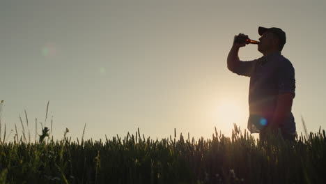 Silhouette-of-a-man-who-drinks-beer-against-the-background-of-a-wheat-field-where-the-sun-sets
