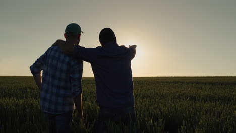 A-man-and-his-son-watch-the-sunrise-over-a-wheat-field-together.-Farmers-in-the-field-and-family-business