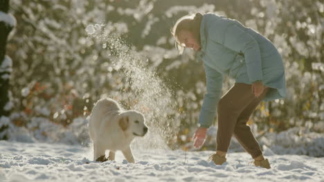 Mujer-De-Mediana-Edad-Divirtiéndose-En-Winter-Park---Arrojando-Nieve-A-Su-Perro-Golden-Retriever