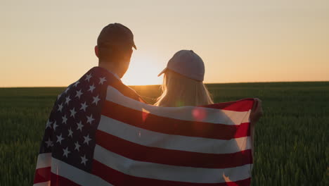 Zwei-Bauern-Mit-Der-US-Flagge-Auf-Den-Schultern-Beobachten-Den-Sonnenuntergang-über-Einem-Weizenfeld.