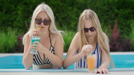 Mom-and-teenage-daughter-relax-by-the-pool,-drinking-cocktails