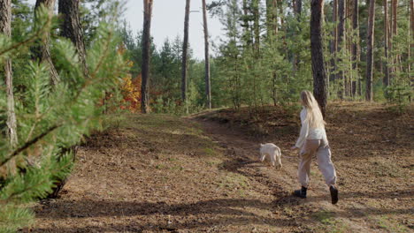 A-teenage-girl-runs-with-a-dog-along-a-path-in-a-pine-forest.