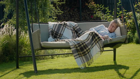 An-elderly-woman-sleeps-in-a-garden-swing-in-the-backyard-of-a-house