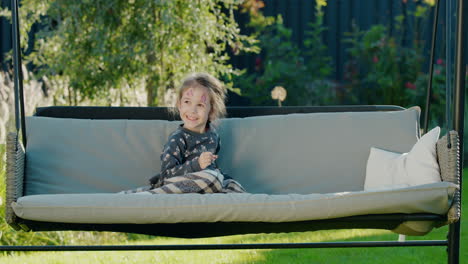 Portrait-of-a-cute-girl-with-face-painting-on-her-face,-resting-in-the-backyard-of-a-house-in-a-garden-swing