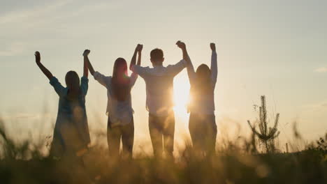 Silhouette-of-a-group-of-friends---raise-their-hands-up-against-the-backdrop-of-the-setting-sun.-Teamwork-and-success-concept