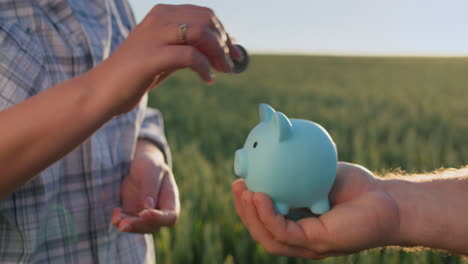 A-woman's-hand-puts-coins-in-a-piggy-bank-held-by-her-husband.-Family-budget-concept