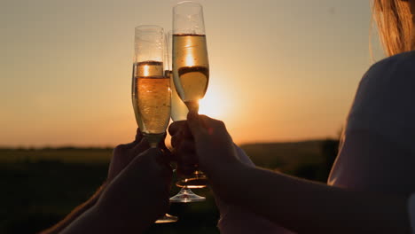 Hands-with-glasses-of-champagne-clink-against-the-backdrop-of-a-picturesque-landscape-where-the-sun-sets