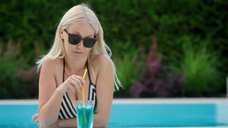 Attractive-young-woman-is-relaxing-by-the-pool,-drinking-a-cool-cocktail.