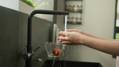 Frauenhände-Waschen-Eine-Reife-Rote-Tomate-Unter-Den-Wasserstrahlen-Aus-Dem-Küchenhahn