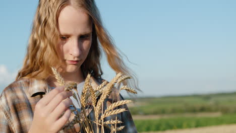 Portrait-of-a-teenage-girl-with-spikelets-of-wheat-in-her-hand.-Stands-against-the-backdrop-of-picturesque-countryside-and-wheat-fields