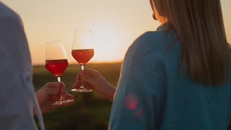 Hands-with-glasses-of-champagne-clink-against-the-backdrop-of-a-picturesque-landscape-where-the-sun-sets