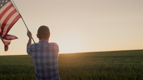 American-farmer-waving-the-US-flag-against-the-backdrop-of-a-field-of-wheat-where-the-sun-rises